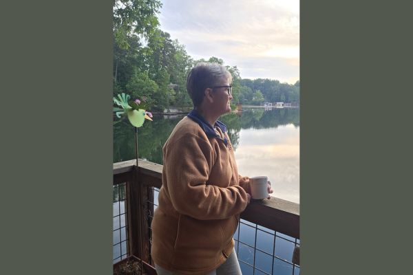 Claudette Eames enjoying a quiet morning with a cup of coffee overlooking a peaceful lake, reflecting on rebuilding calm and strength through intentional moments of stillness.