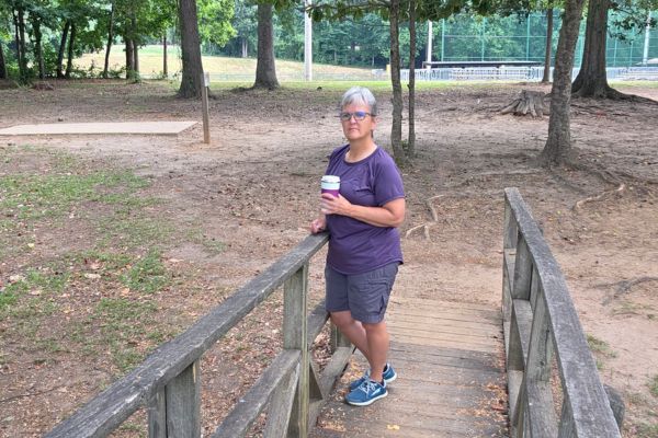 Claudette Eames standing on a wooden bridge surrounded by trees, reflecting the journey of taking the next step when life changes.