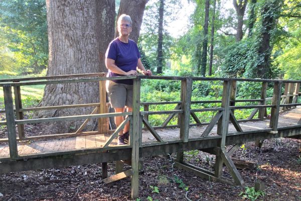 Claudette Eames standing on a wooden bridge surrounded by mature trees during a peaceful morning walk, reflecting on rebuilding calm, strength, and choosing yourself again.