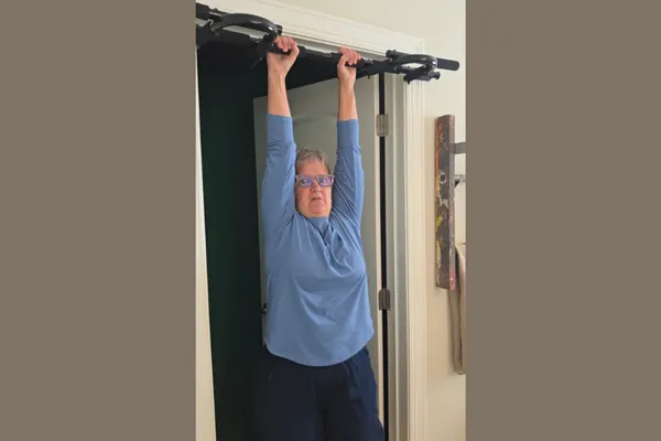 Claudette Eames hanging from a doorway pull-up bar to rebuild her grip strength.