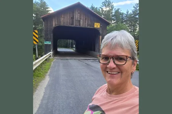 Claudette Eames standing on a country road in front of a covered bridge