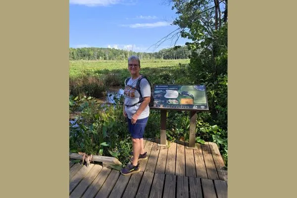 Claudette Eames hiking on a nature trail with a backpack beside a wetland overlook.