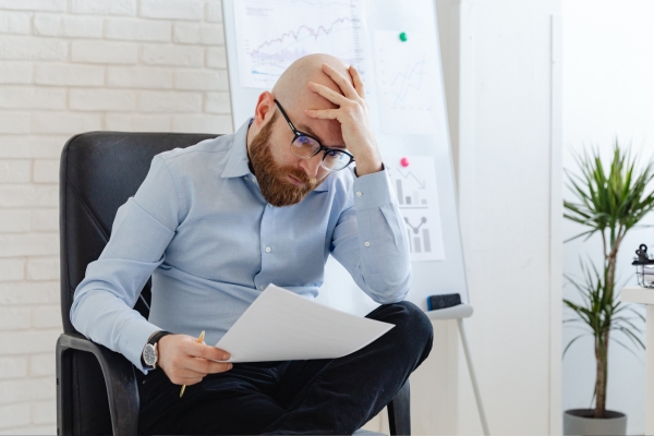 Stressed man looking at report with head in hand