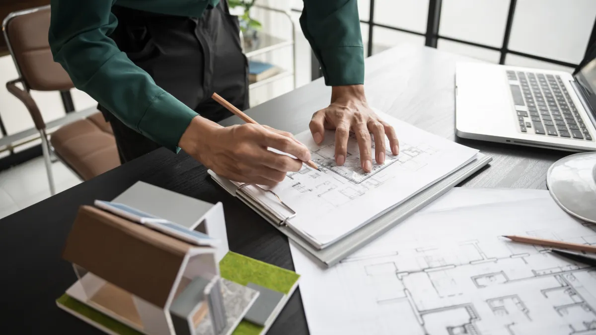 Architect reviewing floor plans with a building model and laptop on the desk