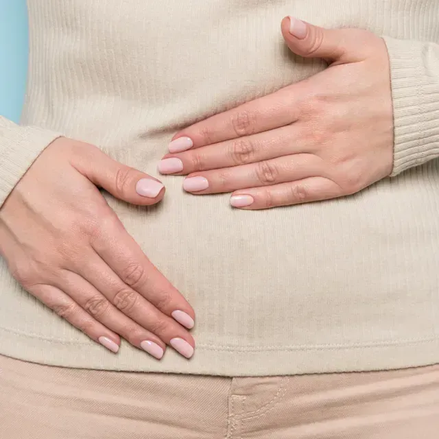 Woman placing both hands on her abdomen, representing bloating and discomfort from progesterone intolerance