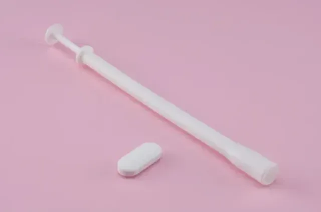 Vaginal suppository applicator and tablet on a pink background, used for treating bacterial vaginosis