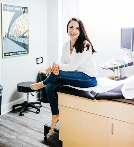 Dr. Carolyn Moyers sitting on exam table in Sky Women’s Health clinic, representing trusted OBGYN care in Fort Worth