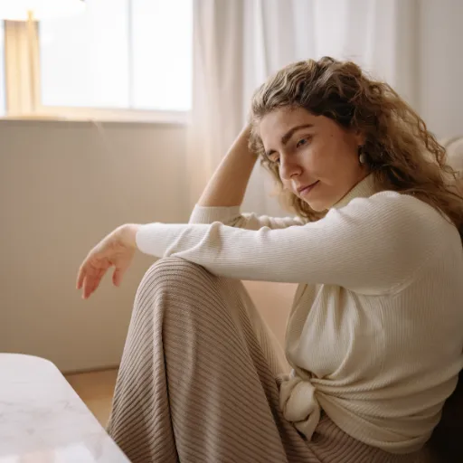 👉 Woman sitting by window in quiet reflection, representing poverty mindset and internal relationship with money
