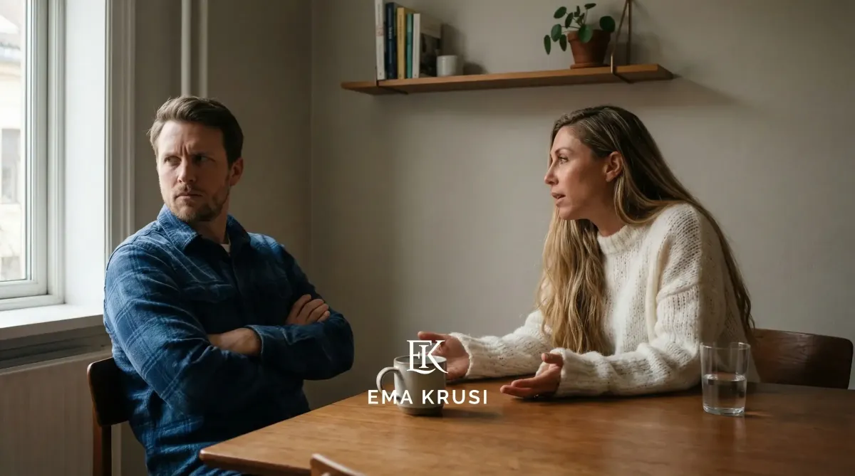 Couple en tension à table : homme bras croisés regardant par la fenêtre, femme parlant avec inquiétude, scène de dispute à la maison.