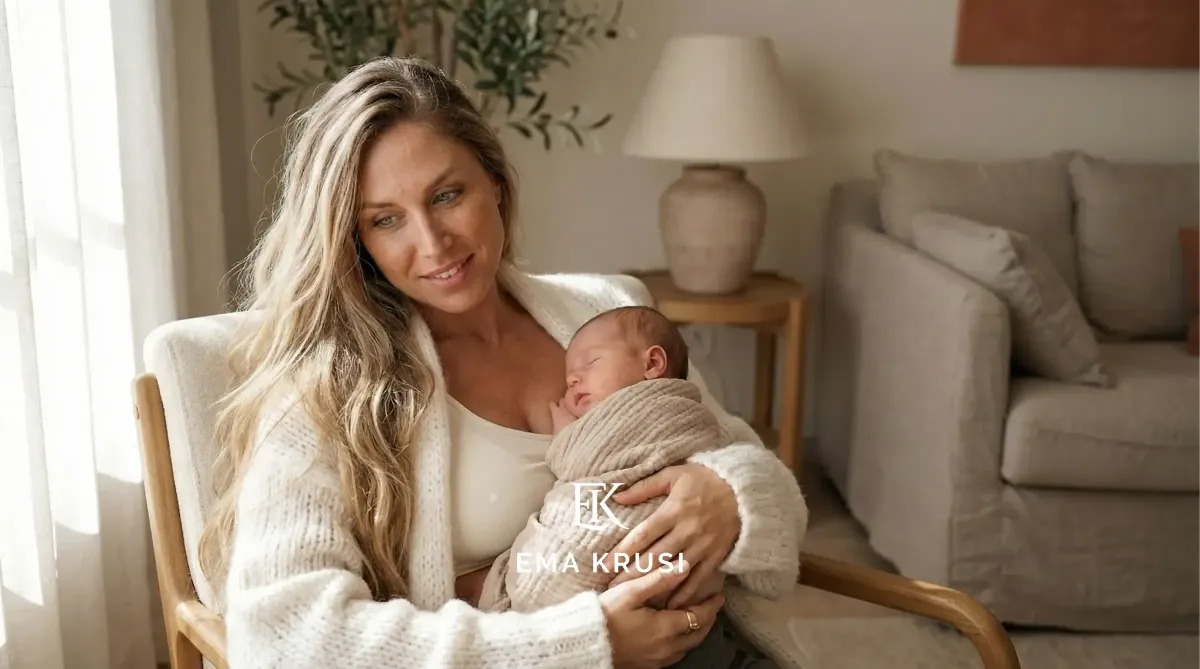 Mère assise dans un fauteuil, berçant un nouveau-né endormi emmailloté, dans un salon lumineux et chaleureux.