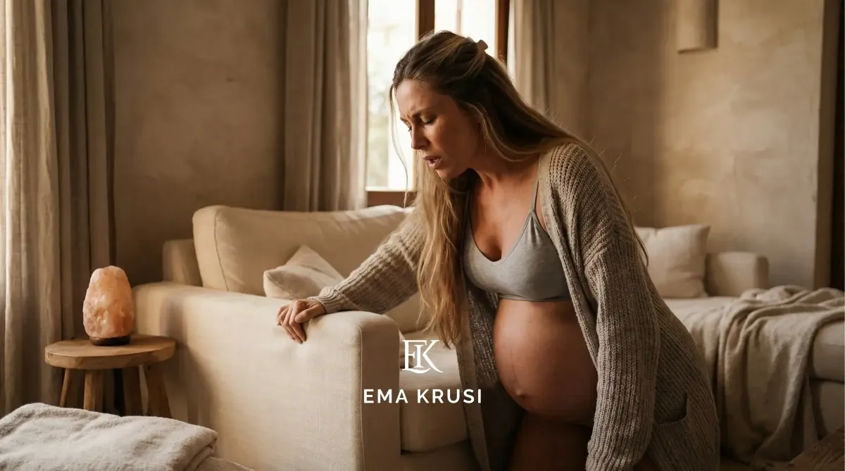 Femme enceinte en travail s’appuyant sur un canapé, respiration intense, dans un salon aux tons chauds.