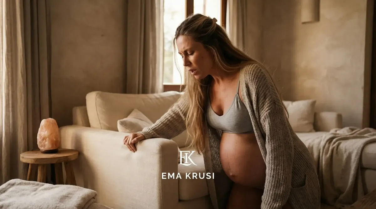 Femme enceinte en travail à la maison, appuyée sur un canapé pour gérer les contractions avant l’accouchement.