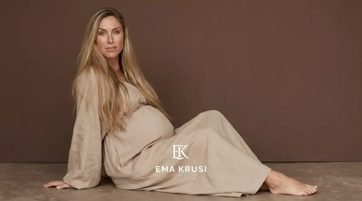 Portrait d'une femme enceinte en robe en lin sur fond uni brun, illustrant la confiance, la sérénité et la beauté naturelle de la grossesse dans un style minimaliste.
