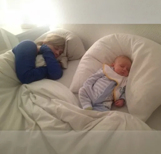 Un nouveau-né endormi sur un coussin d’allaitement, sur un grand lit blanc
