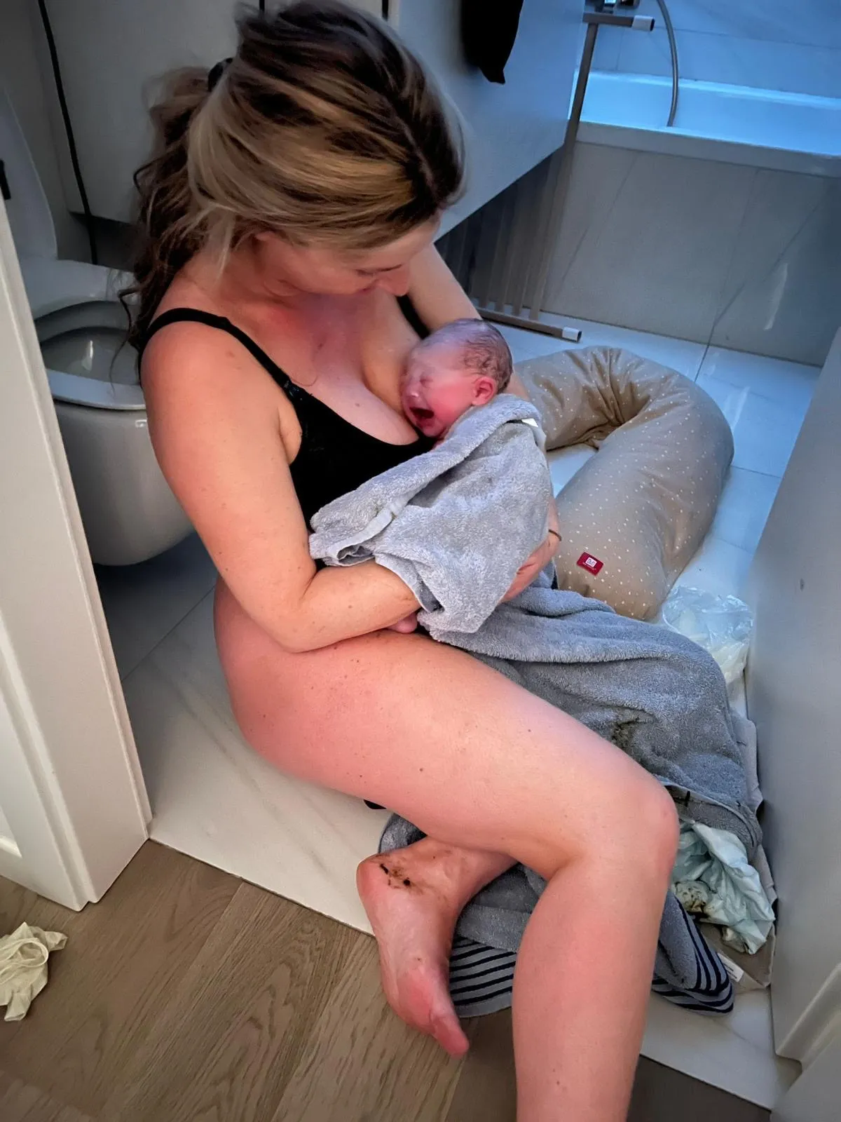 Une maman assise par terre dans sa salle de bain, son nouveau-né contre elle