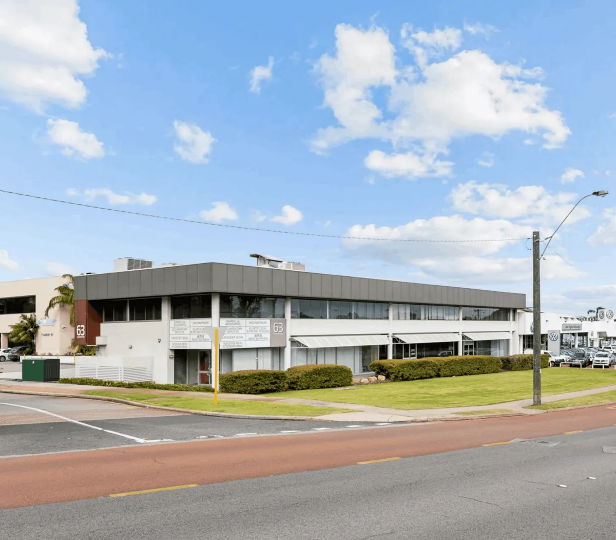 Bright interior photo showing a furnished serviced office in a suburban coworking building: warm timber desks, neutral upholstery, plants, and natural daylight from large windows; photorealistic and inviting.