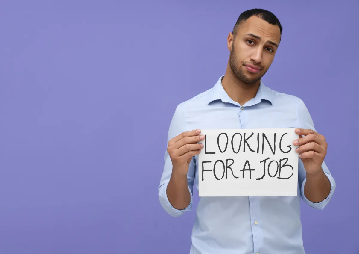 A young professional holding a "Looking for a job" sign against a purple background, representing unemployment and the job search process.
