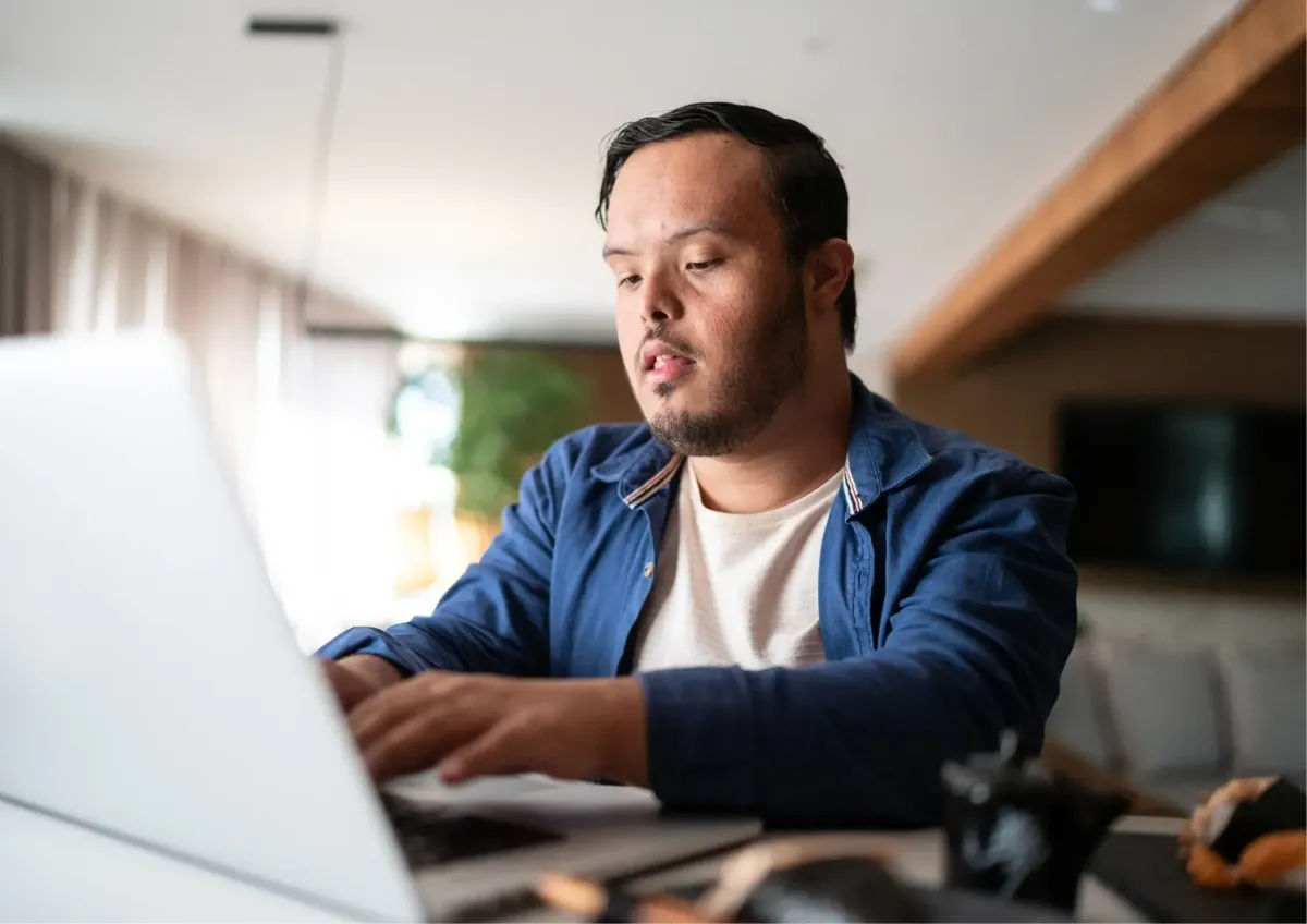 A young male professional with a disability typing on a silver laptop, representing inclusive career opportunities and digital accessibility.