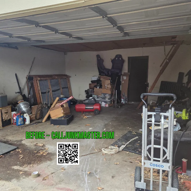 Cluttered garage interior with boxes, tools, and furniture, showcasing a disorganized space before cleanout by Junk Master, featuring visible branding and a QR code for scheduling services.
