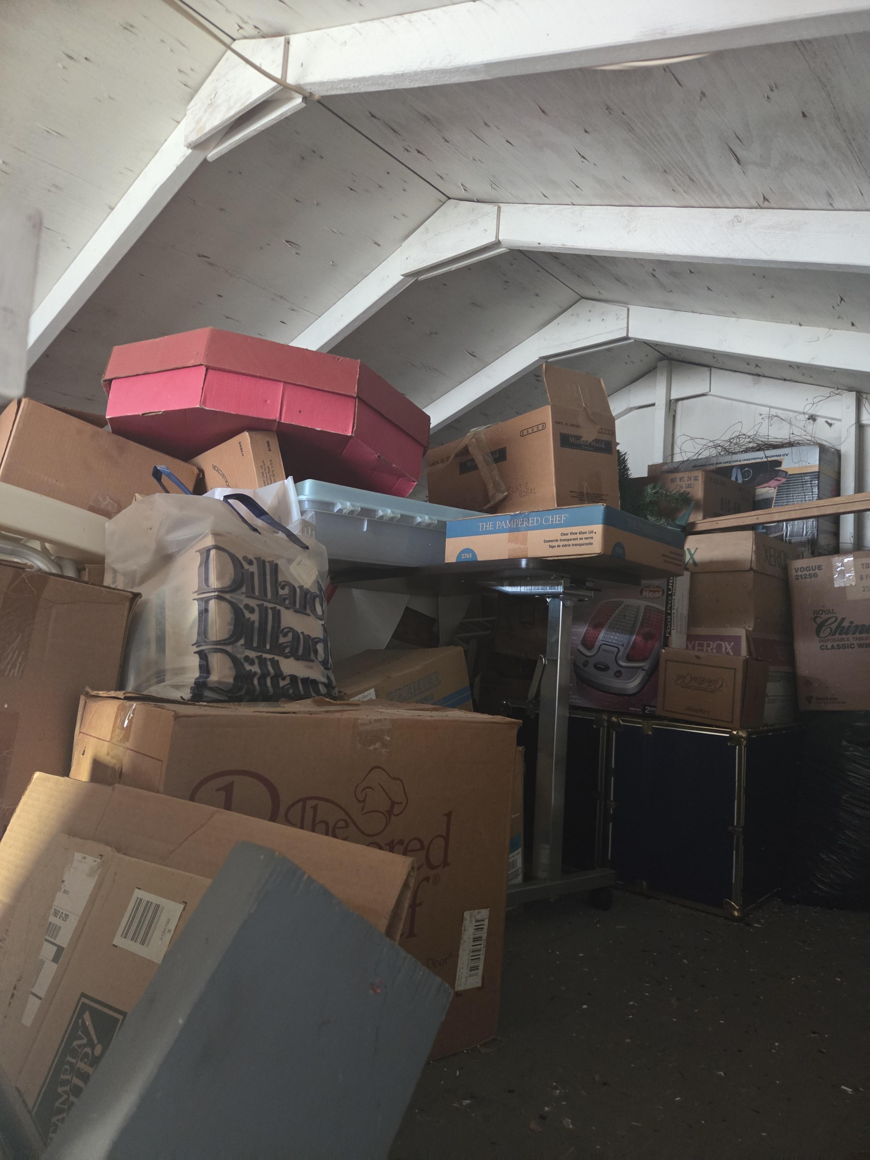 Attic interior filled with old boxes, furniture, and nautical equipment, showcasing wooden beams and a lifebuoy, emphasizing clutter and potential for cleanout services.