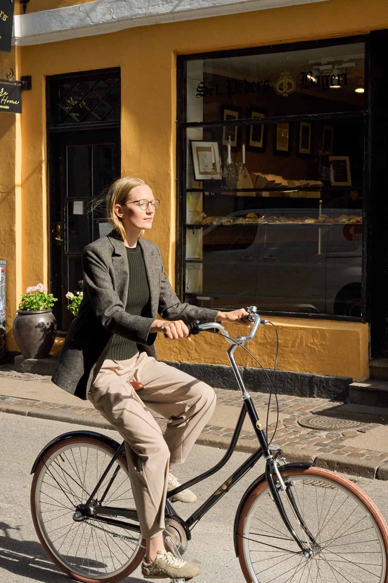 Woman wearing ProDesign eyeglasses while riding a bicycle through a sunny city street.