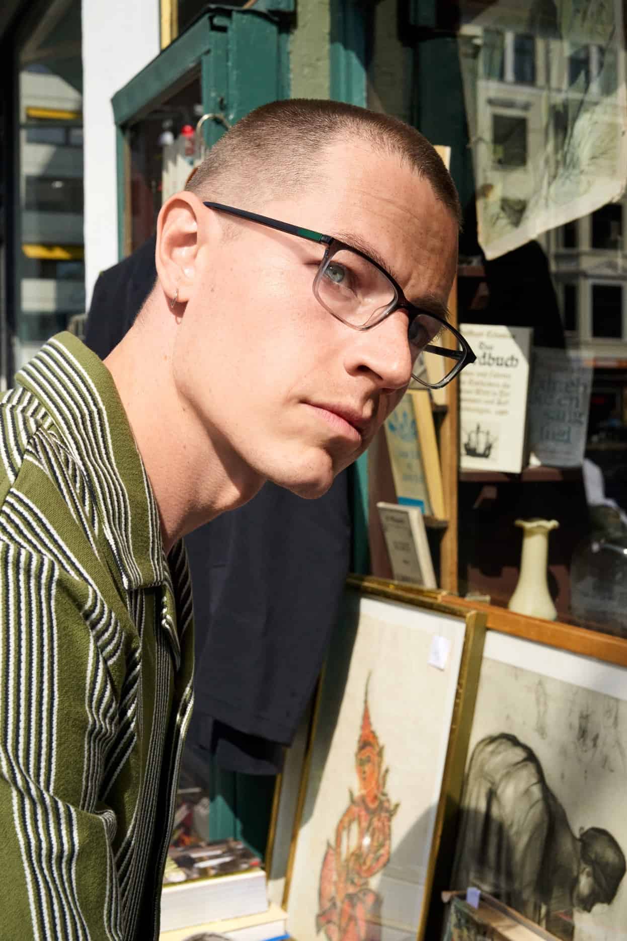Man wearing black ProDesign eyeglasses while browsing artwork outside a city shop.