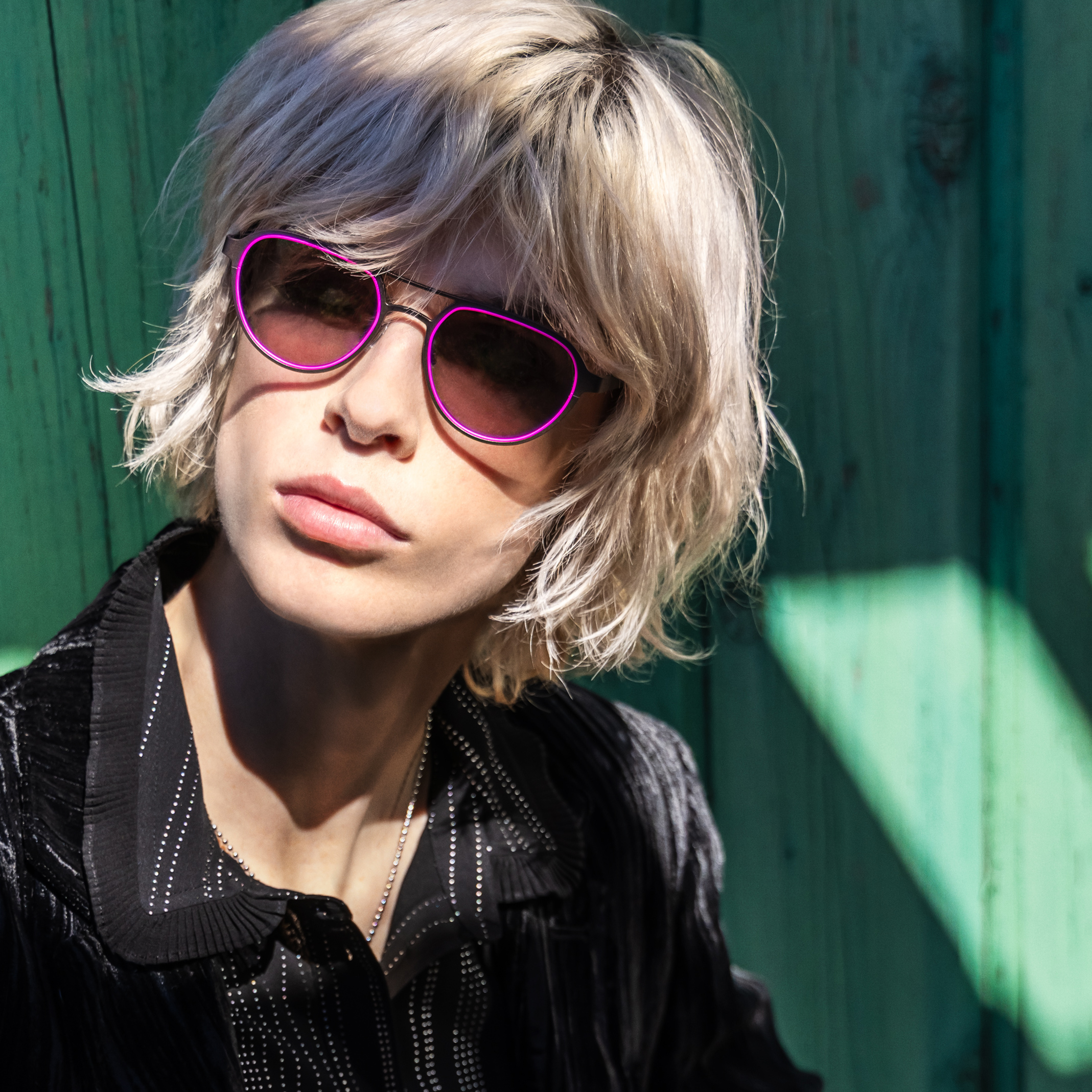 Model wearing purple oval Bevel sunglasses against a green wooden background.