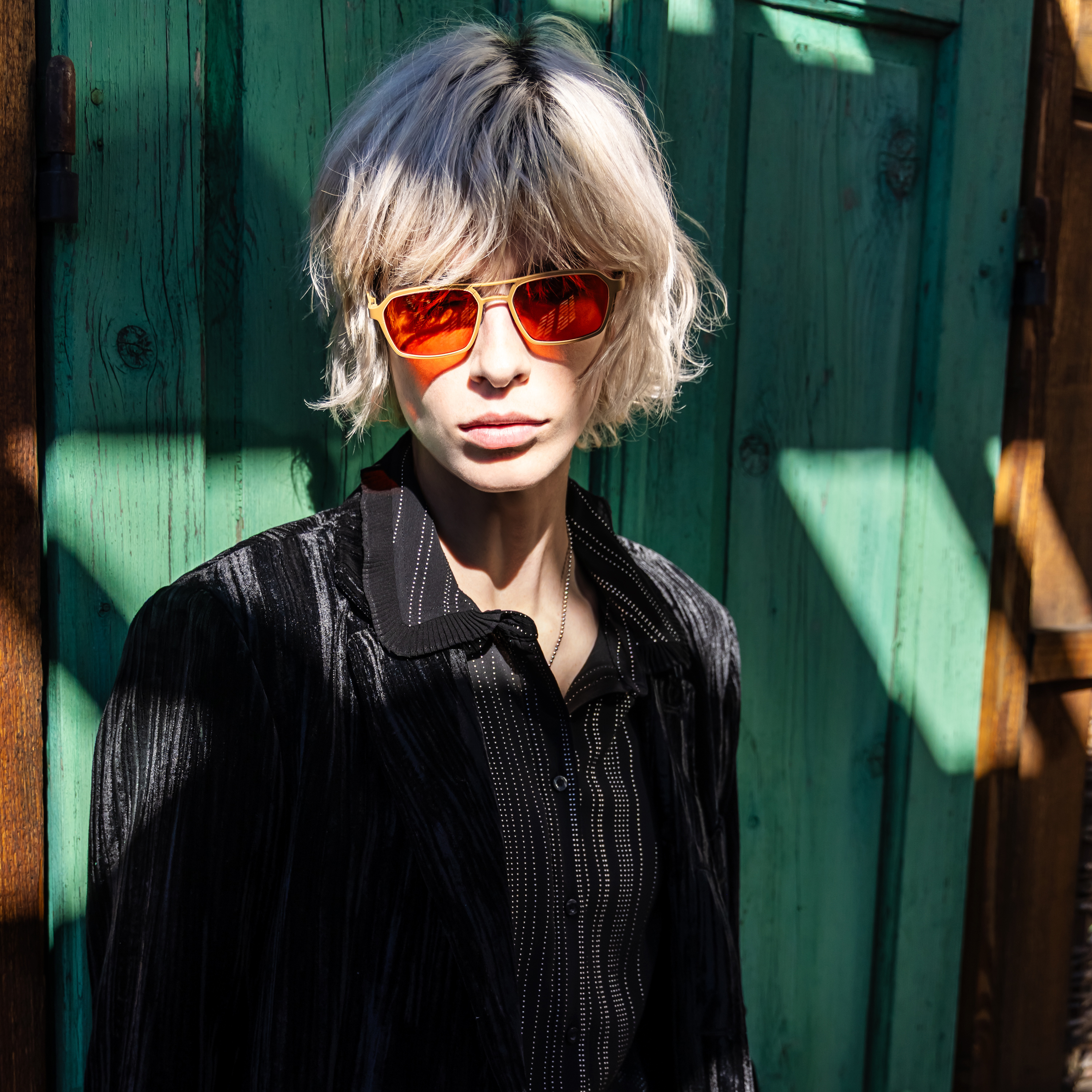 Model wearing bold red Bevel sunglasses against a rustic green wooden background.