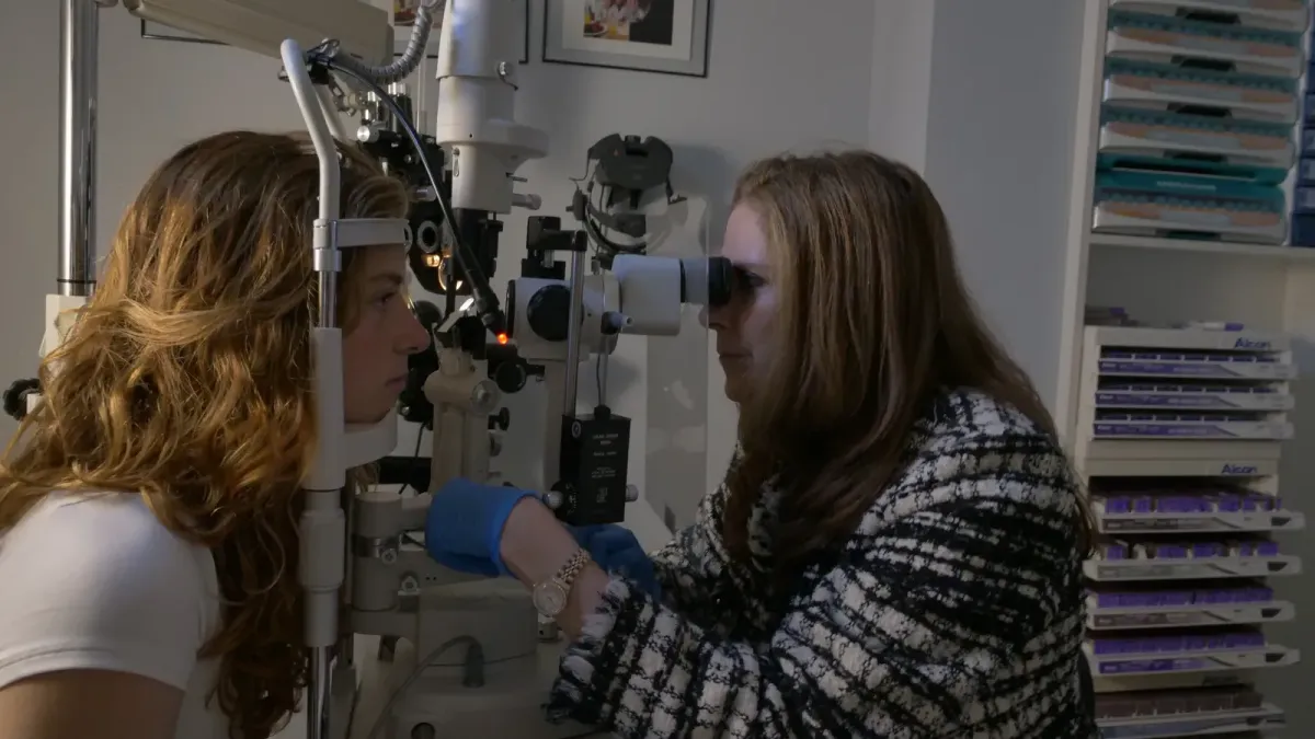 Dr. Michelle Blas examining a patient with a slit lamp at Eyes in Disguise Optometry.