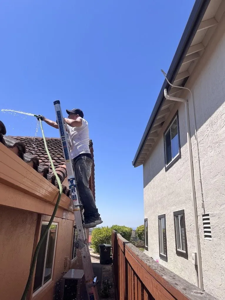 Professional gutter cleaning technician on ladder residential two-story home Solano County Teodor Window Solar