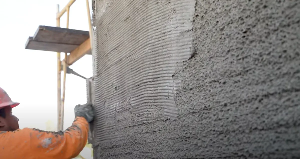 Man in orange shirt and hat applying stucco o a wall 