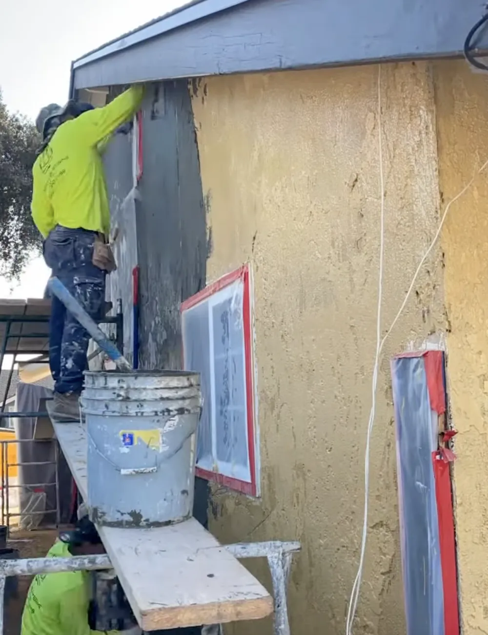 Man in green shirt applying new stucco to a house