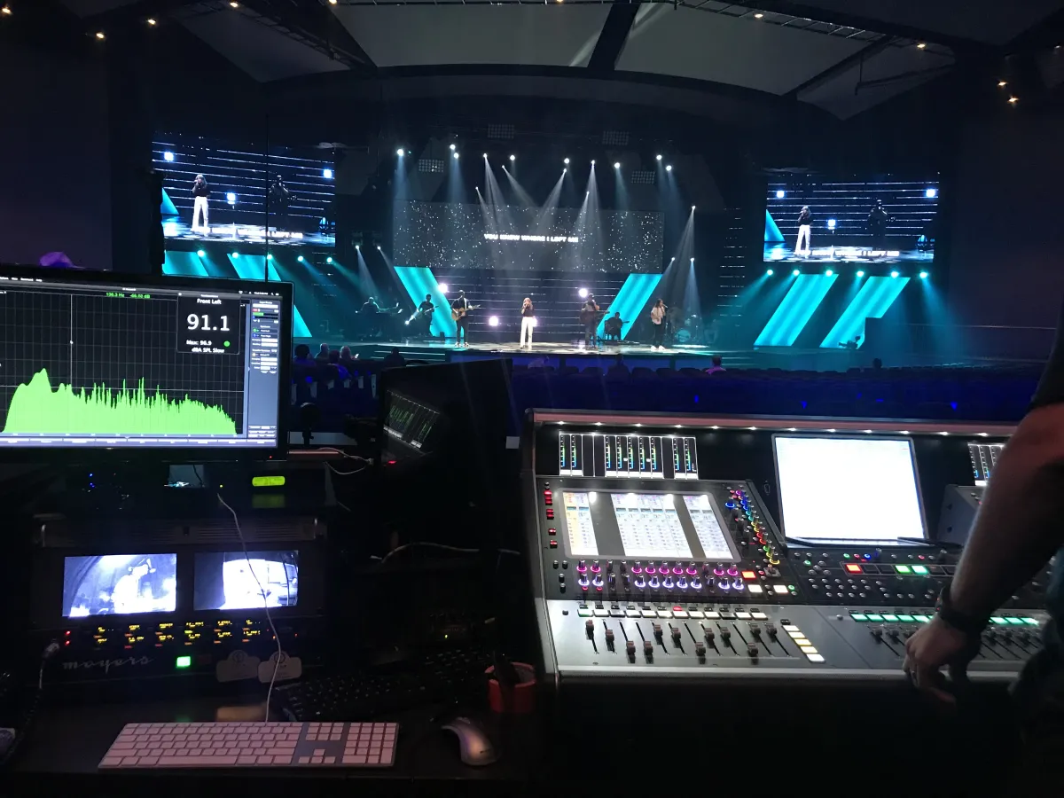 Audio engineer monitoring live worship production with digital metering and stage lighting