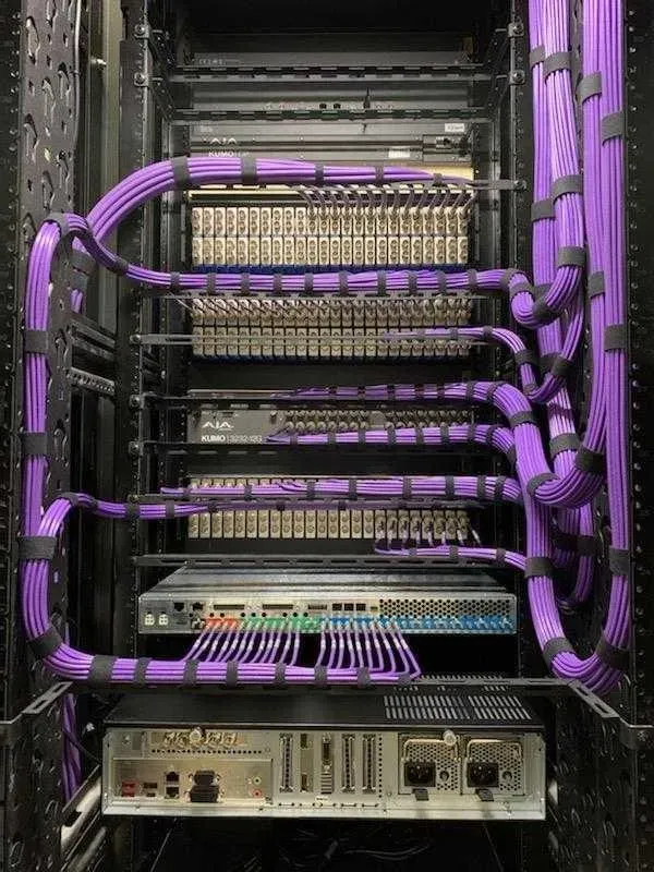 Professional AV equipment rack with neatly organized purple network and audio cables, patch panels, and broadcast gear for church livestream and audio video integration.