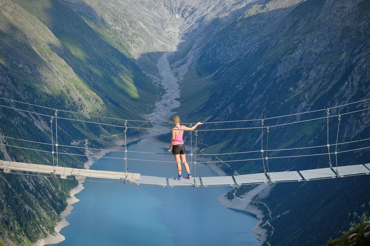 Person stood on a rope bridge overlooking a large river in a valley. 