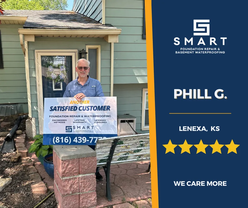 Phill G. from Lenexa, KS smiling and holding a 'Satisfied Customer' sign from SMART Foundation Repair & Basement Waterproofing with a green house background.