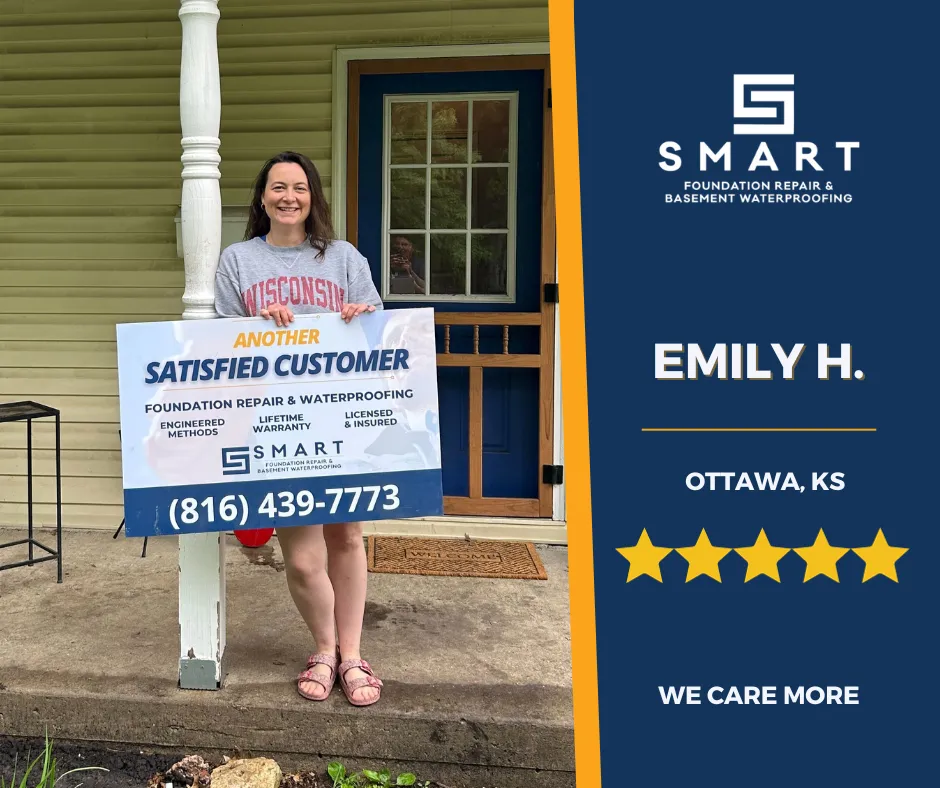 Satisfied customer, Emily H., from Ottawa, KS, proudly holding a sign indicating her positive experience with SMART Foundation Systems for foundation repair and basement waterproofing. The company's logo, contact number, and a 5-star rating emphasize their commitment to quality service with the tagline 'We Care More'.