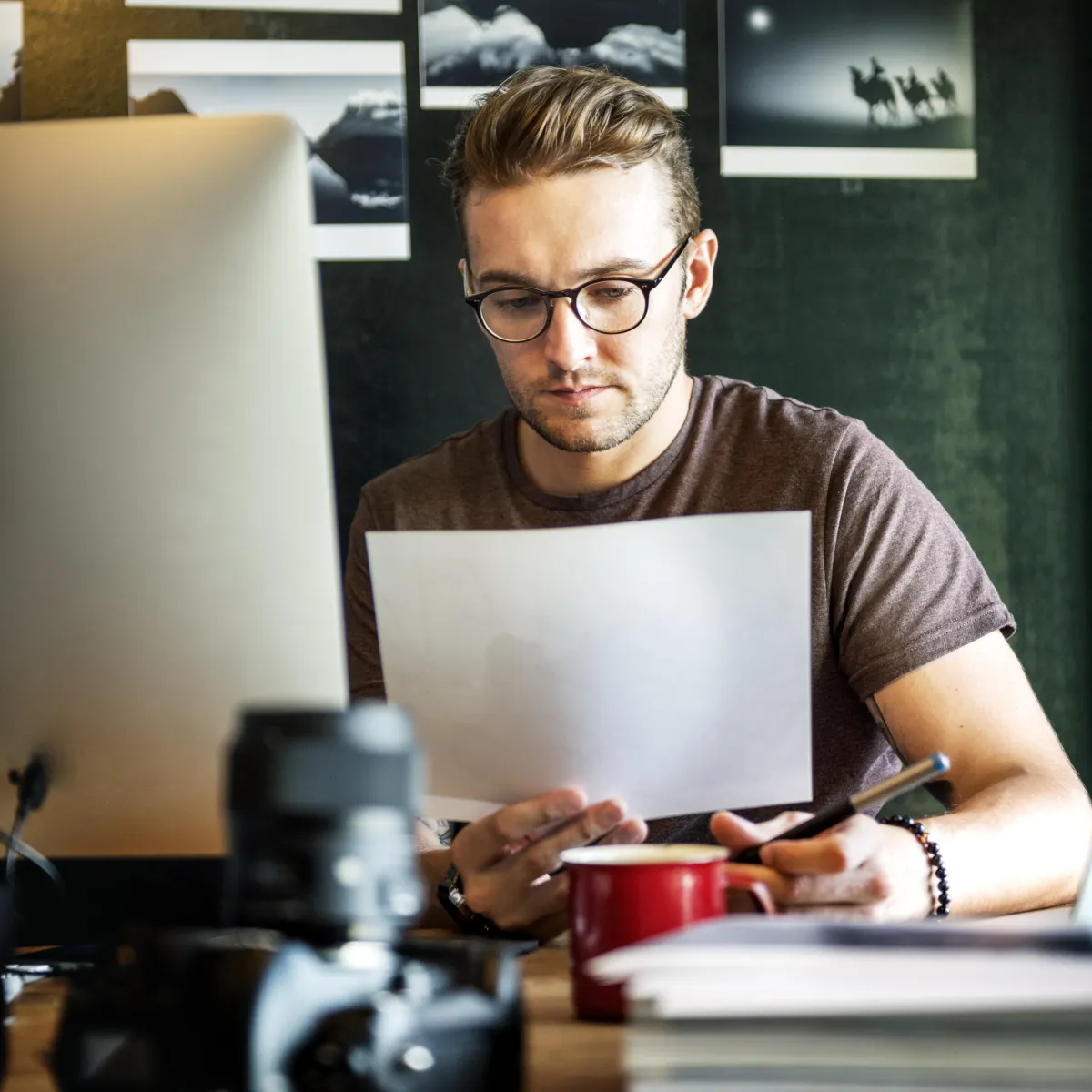 Man reviewing documents at a desk with a computer, camera, and coffee cup, representing focus on lead management and automation for business efficiency.