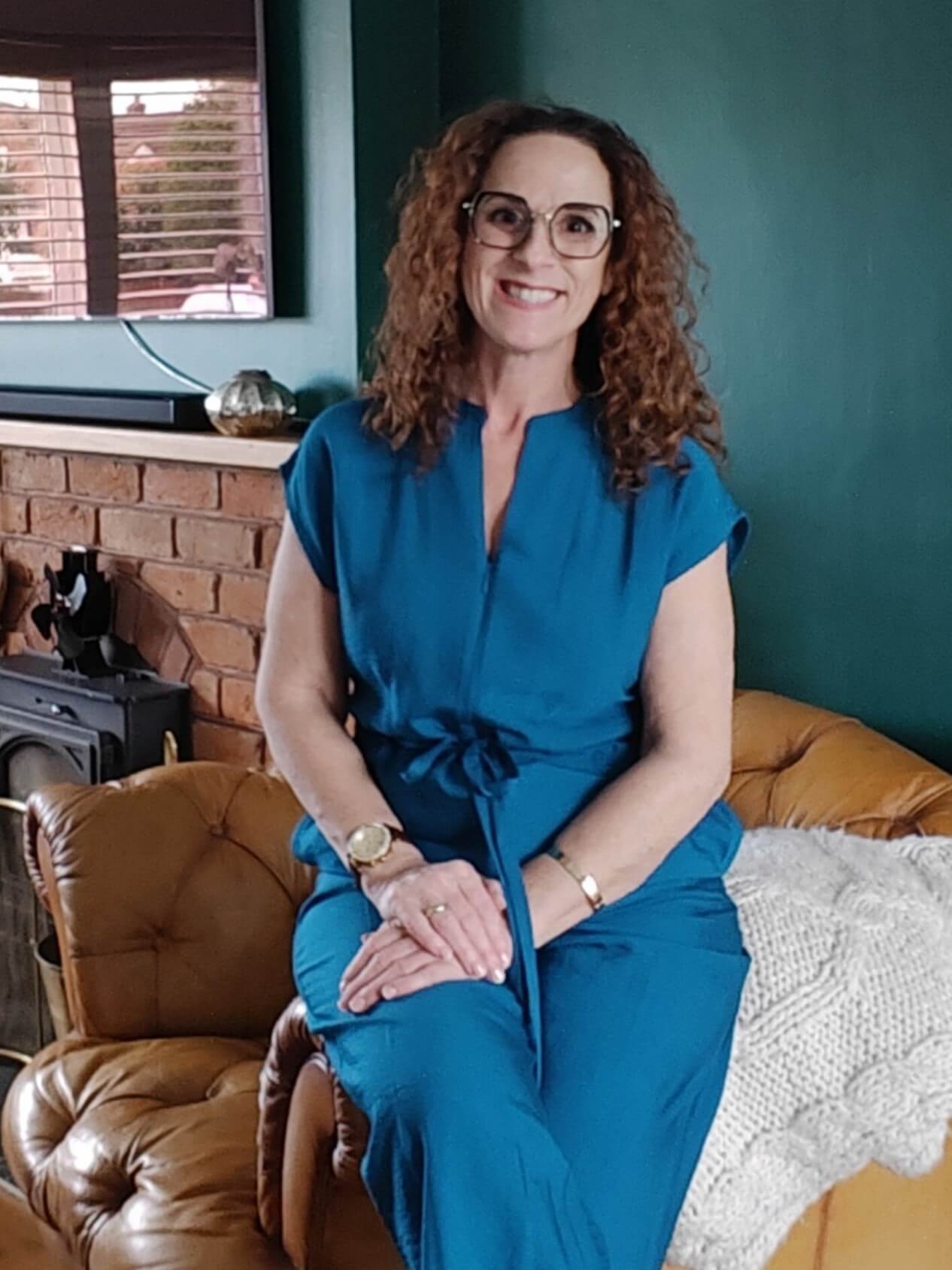 Louise, ethical leadership consultant and creator of the CIVIL Framework, smiling in a teal jumpsuit on a leather sofa