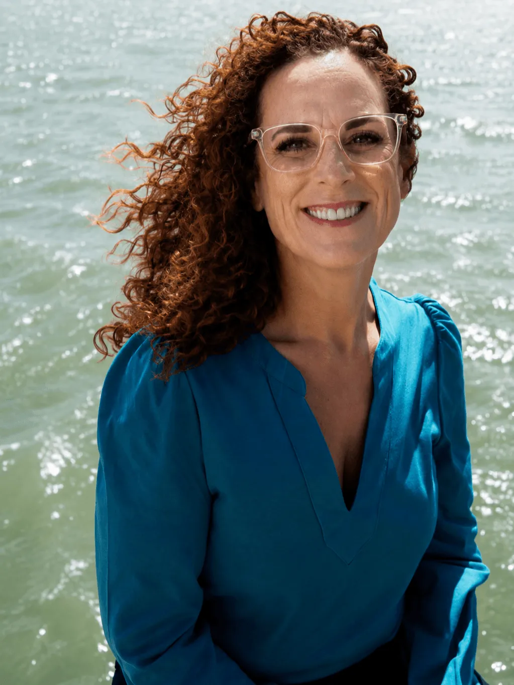 Louise, ethical leadership consultant, smiling outdoors by the water in a teal blouse.