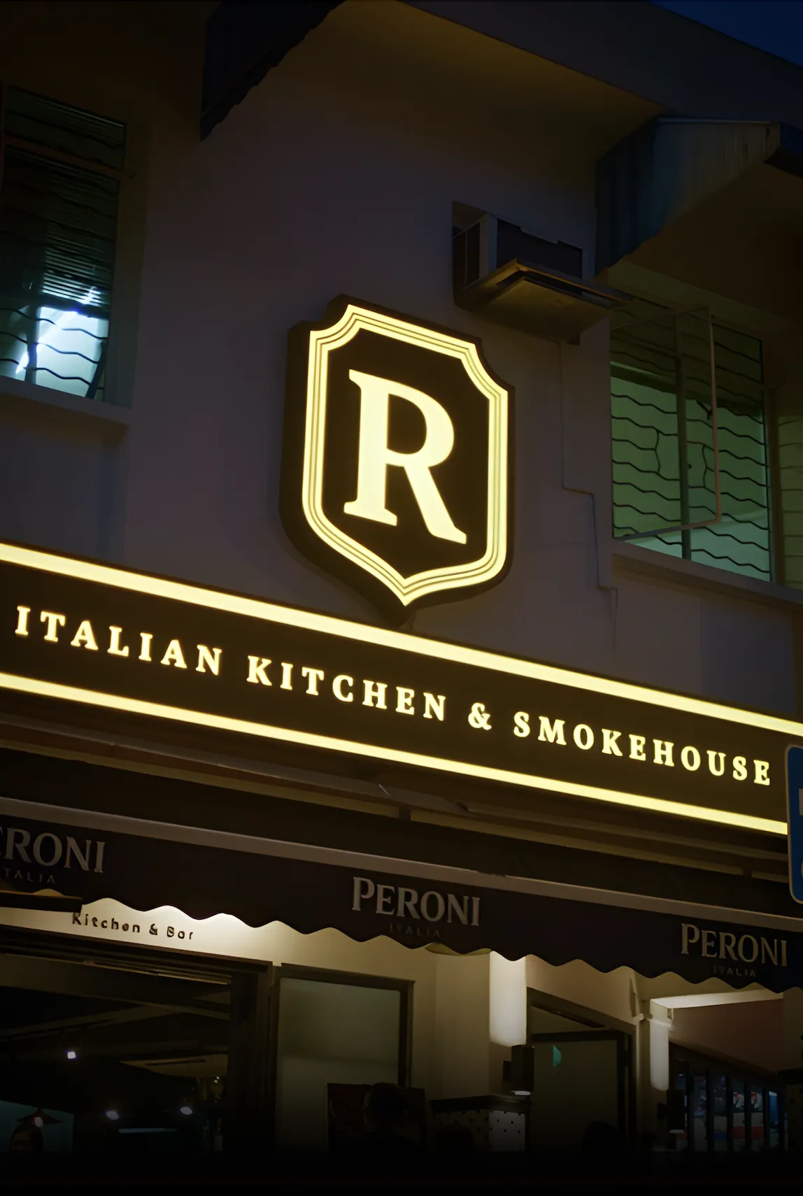 R Italian Kitchen & Smokehouse entrance with illuminated signage at night in Greenwood, Singapore.