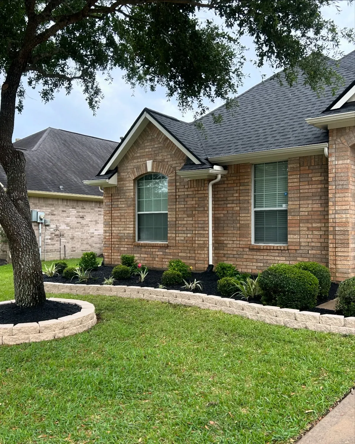 Residential landscaping with flower beds, shrubs, mulch, and stone borders