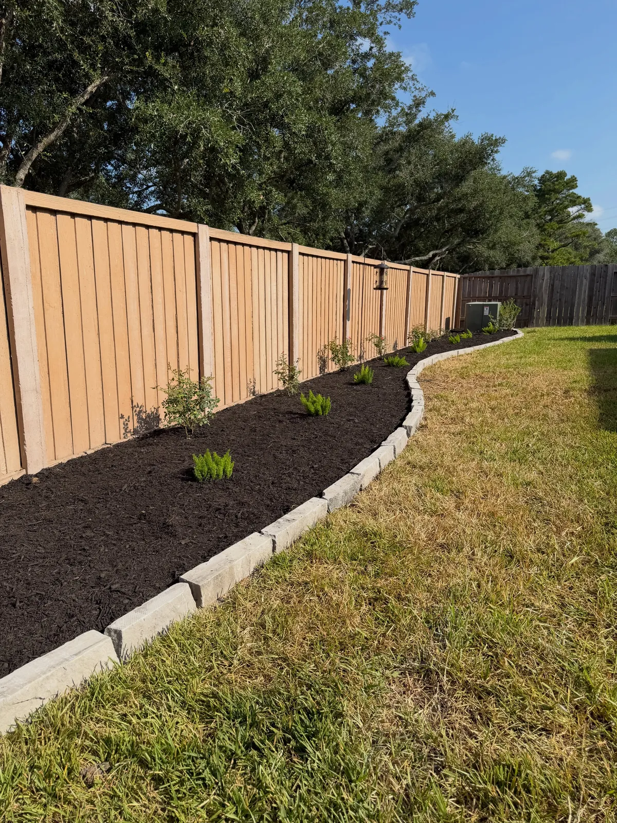 Residential backyard with wooden privacy fence, landscaped flower beds, and stone edging