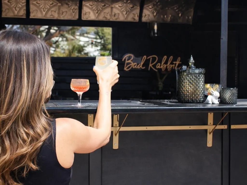 Guest raising a drink at the Bad Rabbit Caravan bar window, highlighting mobile bartender service in Denver