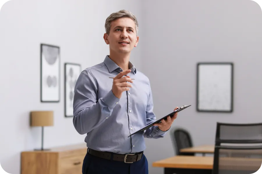 Man holding a clipboard and speaking indoors.
