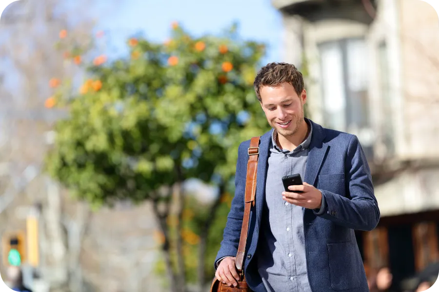 Man walking outdoors while looking at his smartphone.