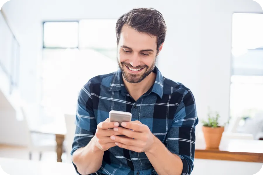 Man smiling while using a smartphone indoors