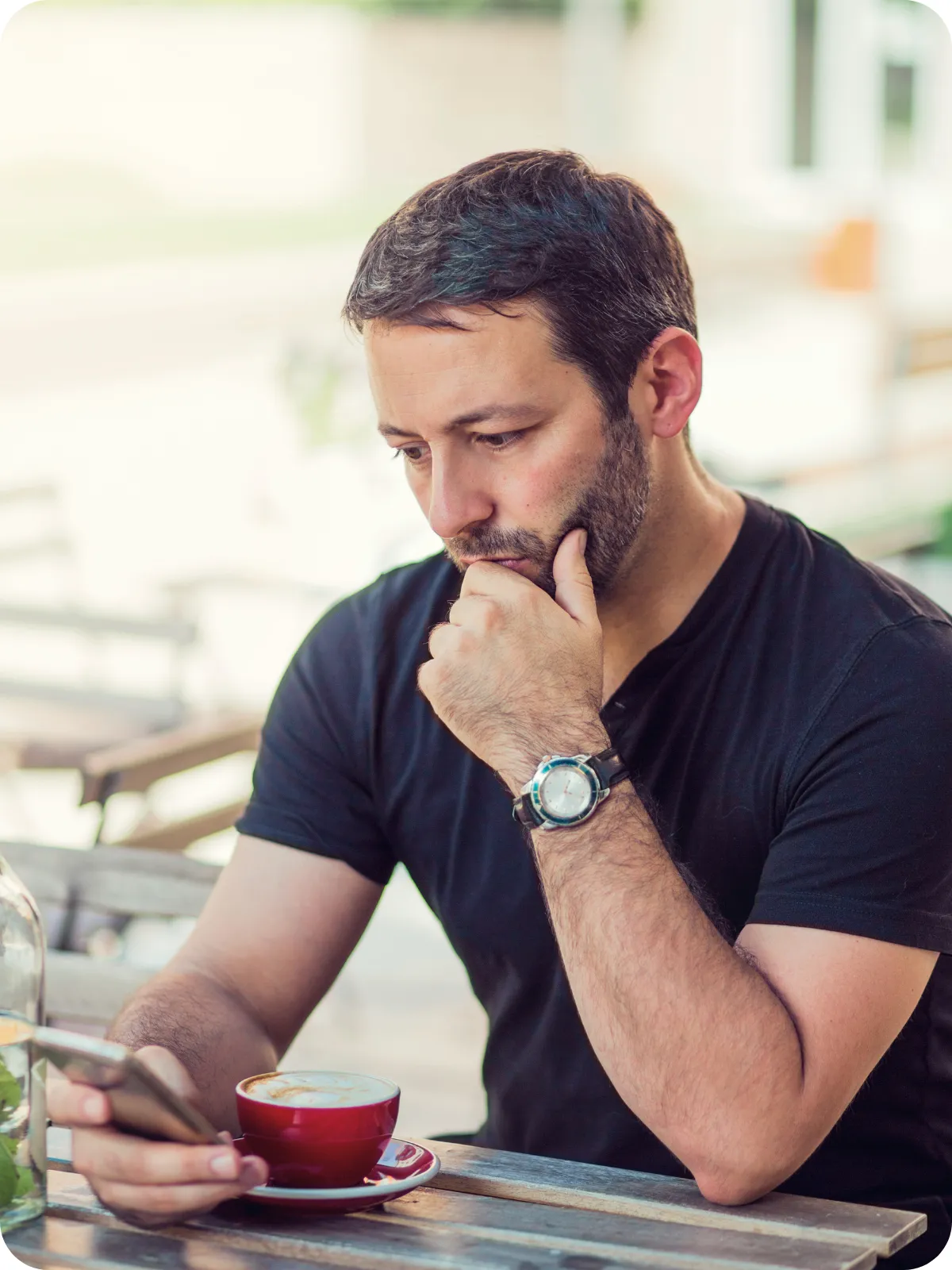 Man sitting at a table looking at his phone with a cup of coffee.