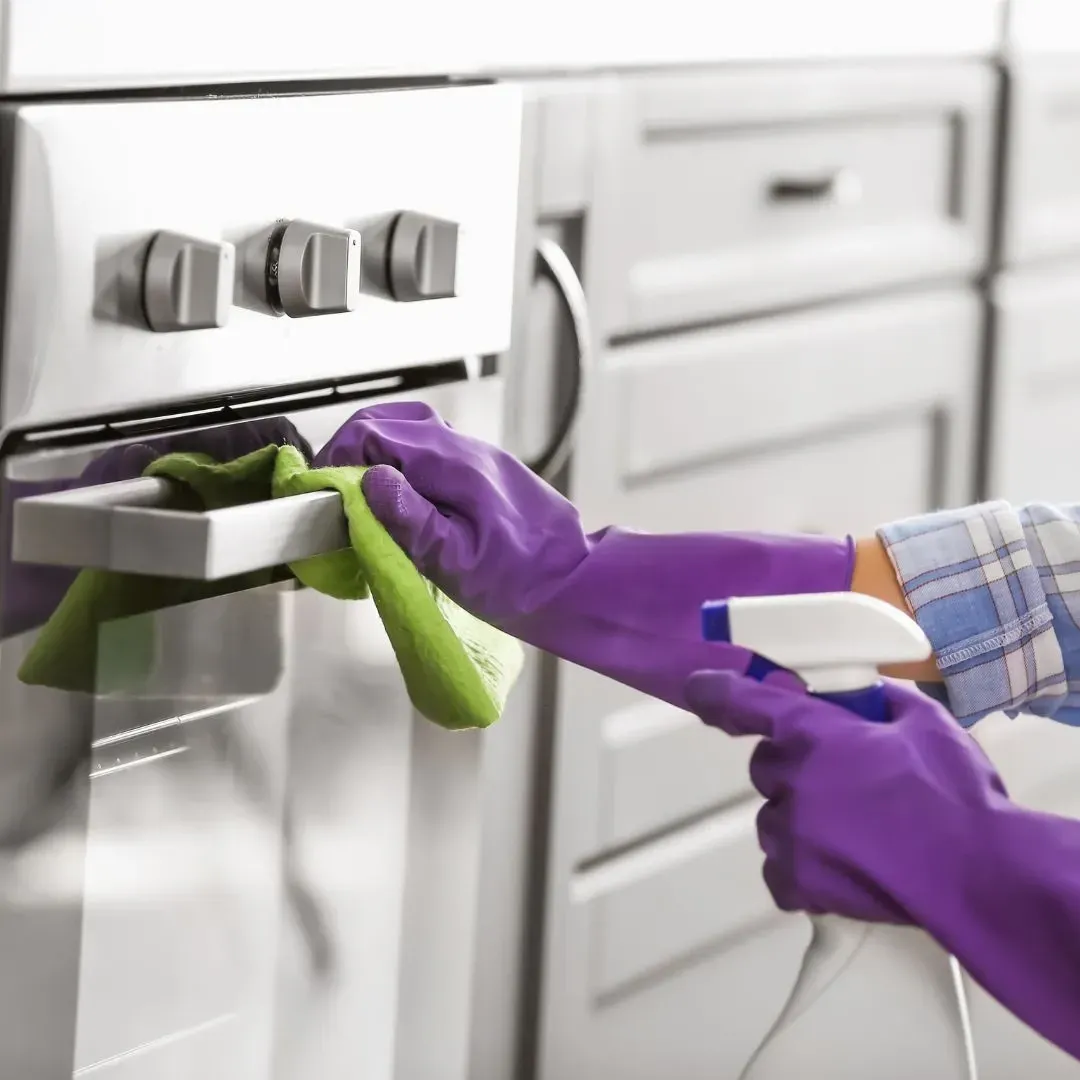 Professional cleaner wearing purple gloves detailing a stainless steel oven, representing deep cleaning services by Maryland Spotless Maid Service.