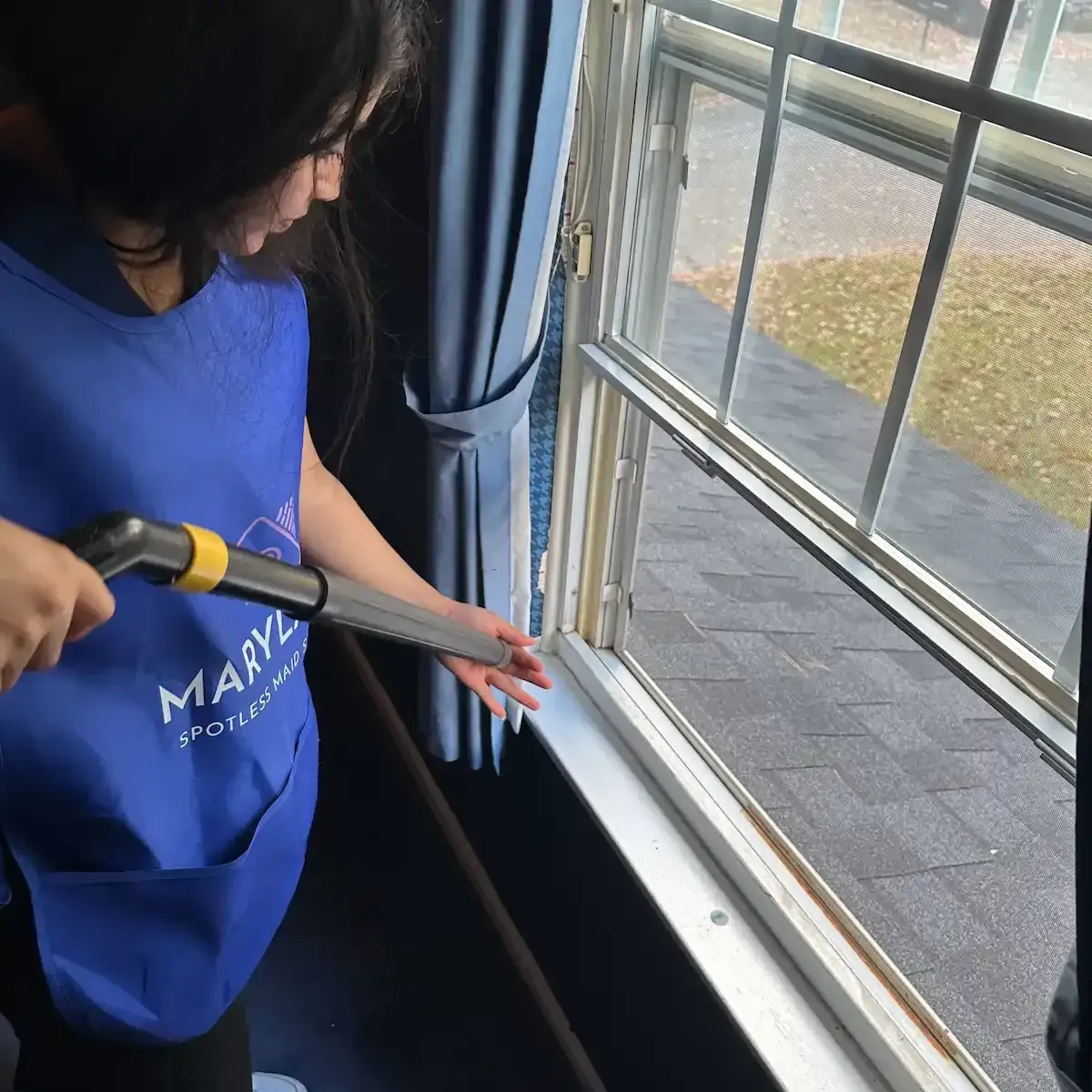Professional maid cleaning a sunlit window sill in a Maryland home, featuring the text 'Enjoy a Spotless Home' and a red 'Book Now' button for residential cleaning services